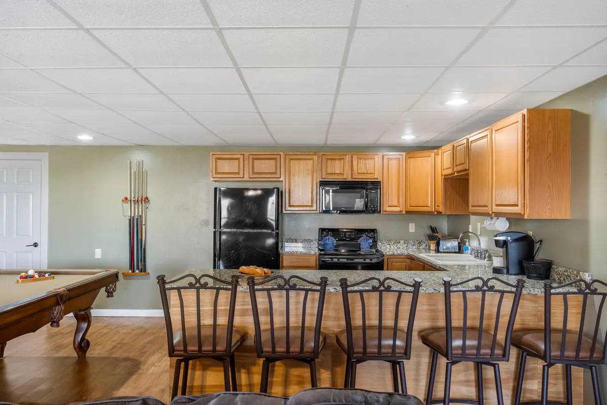 An interior recreation space featuring a kitchen counter, a pool table, bar stools, and a casual, friendly setup. This open-plan area is designed for entertaining, playing games, and socializing—perfect for group tournaments and friendly competitions.
