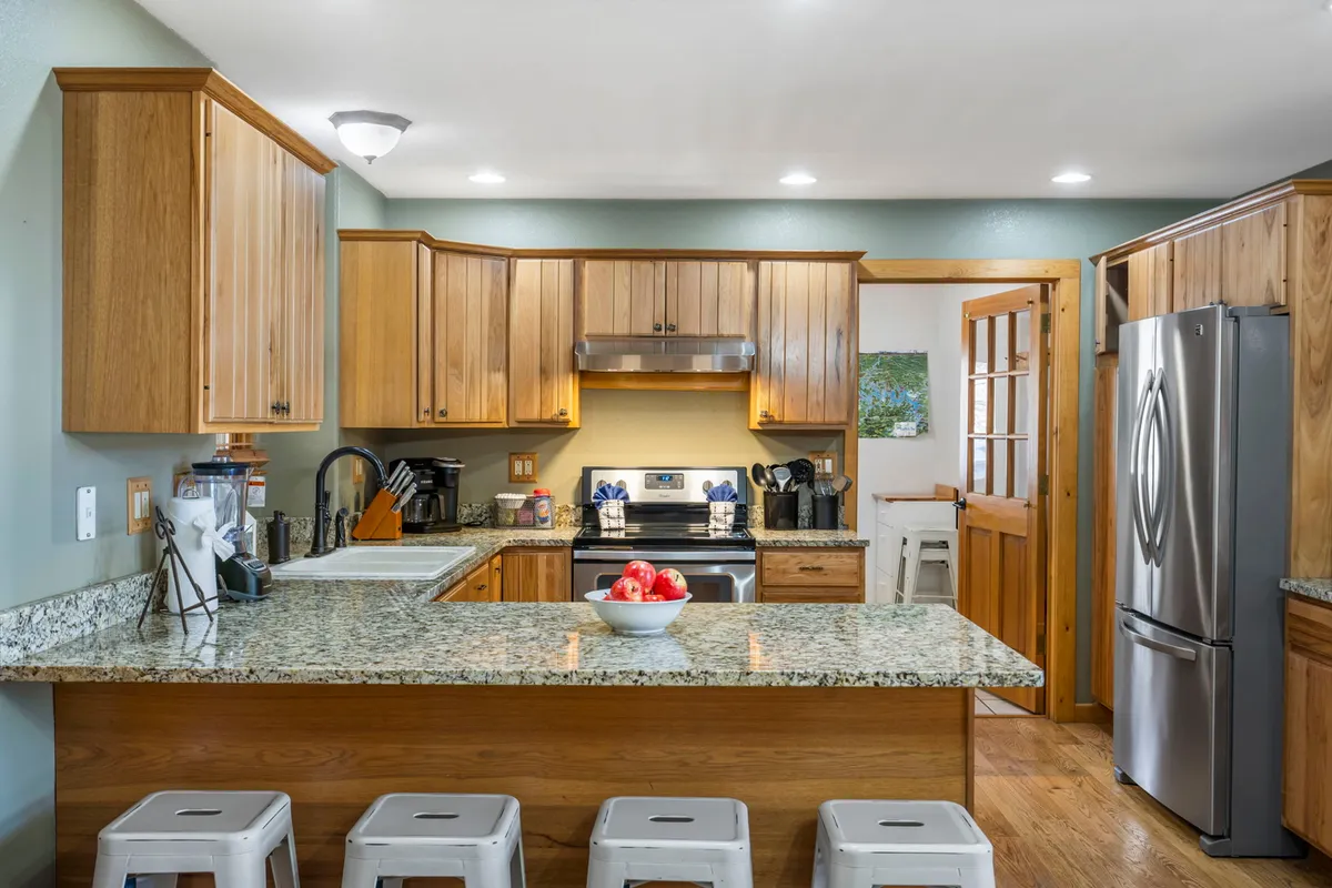 A well-appointed main kitchen with a granite island countertop, stainless steel appliances, wood cabinetry, and ample space for cooking and entertaining. Bright and inviting, the kitchen opens into the main living area, reinforcing the open-concept design.