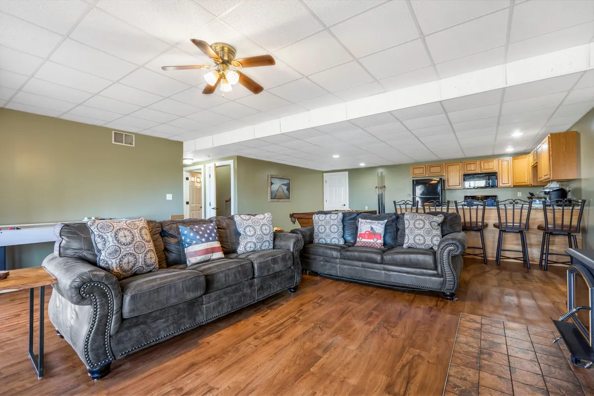 A spacious living area with comfortable sofas, a kitchen in the background, and wood flooring. The setup is ideal for gathering, socializing, or accommodating additional guests with sleeper sofas.