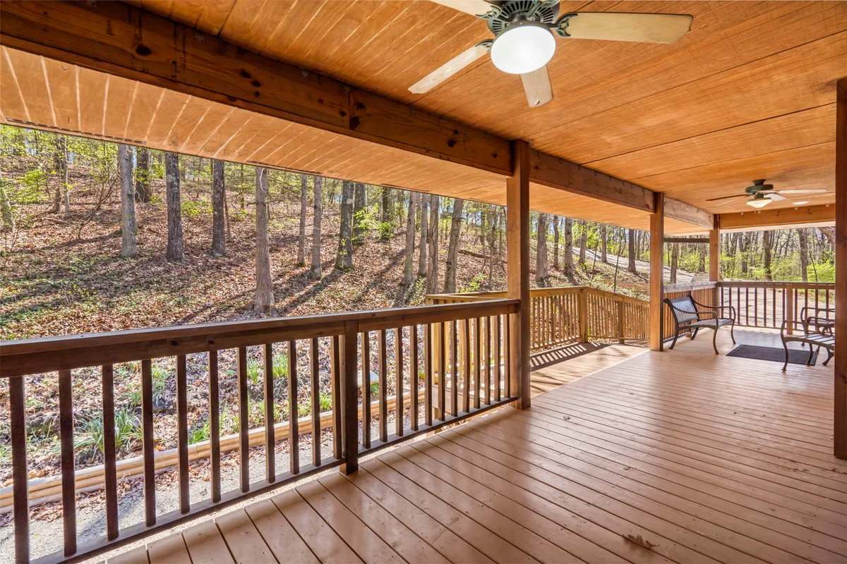 The image highlights a wooden deck surrounded by lush trees, equipped with comfortable outdoor seating and a ceiling fan. The tranquil setting encourages both entertaining guests and peaceful relaxation amid nature.
