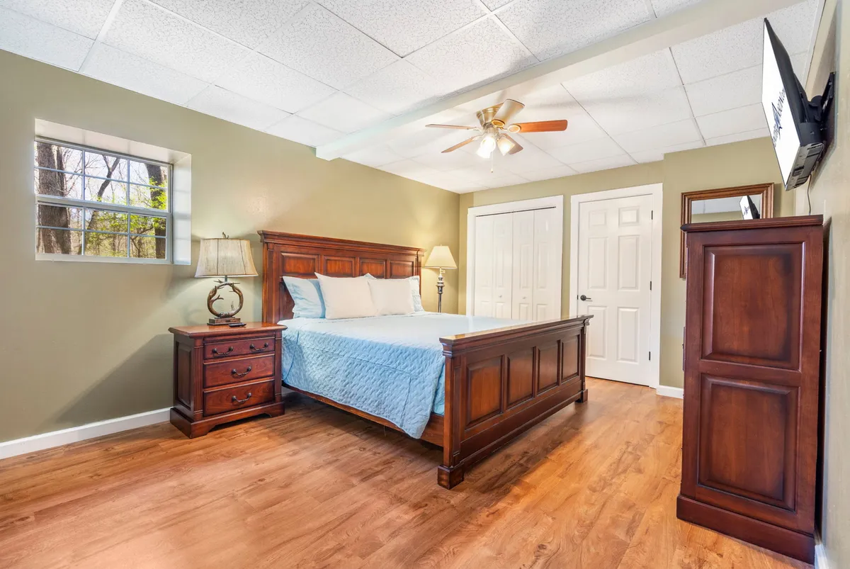 A warmly lit bedroom with a plush king-sized bed, a wooden nightstand with a lamp, a wardrobe, and a window letting in soft natural light. The room radiates comfort and tranquility, ideal for restful mornings or quiet evenings.