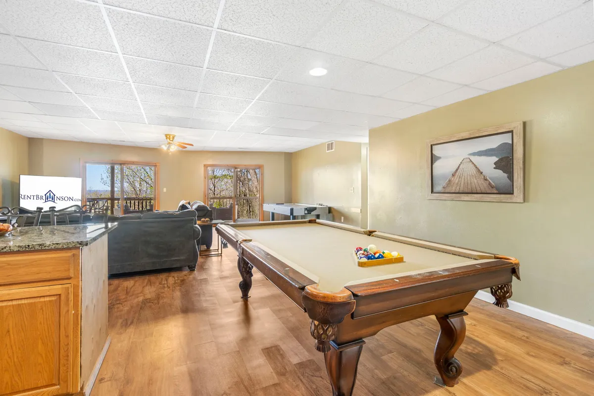 A welcoming interior recreation space featuring a pool table, a bar counter, and large windows that let in natural light. The setup is ideal for family game nights, socializing, and unwinding after a day of outdoor activities.