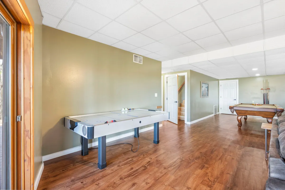 This image features a vibrant recreation room with both an air hockey table and a pool table, set on wooden flooring with an open doorway suggesting a spacious, lively environment. The mood is playful and relaxed, and the layout encourages group activities and friendly competition.